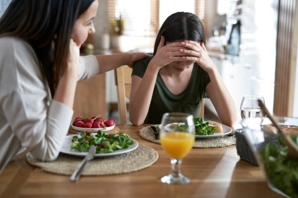 A mother comforts her daughter with disordered eating during a meal.